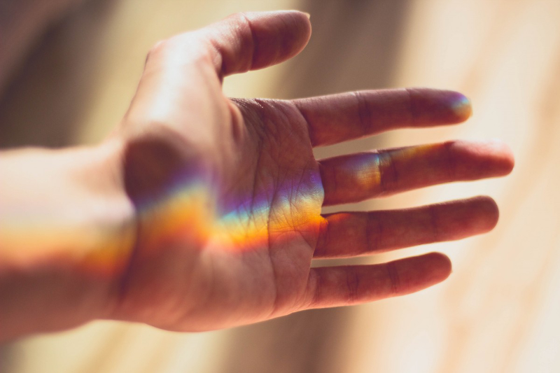 A hand with a rainbow-coloured light shining onto it.